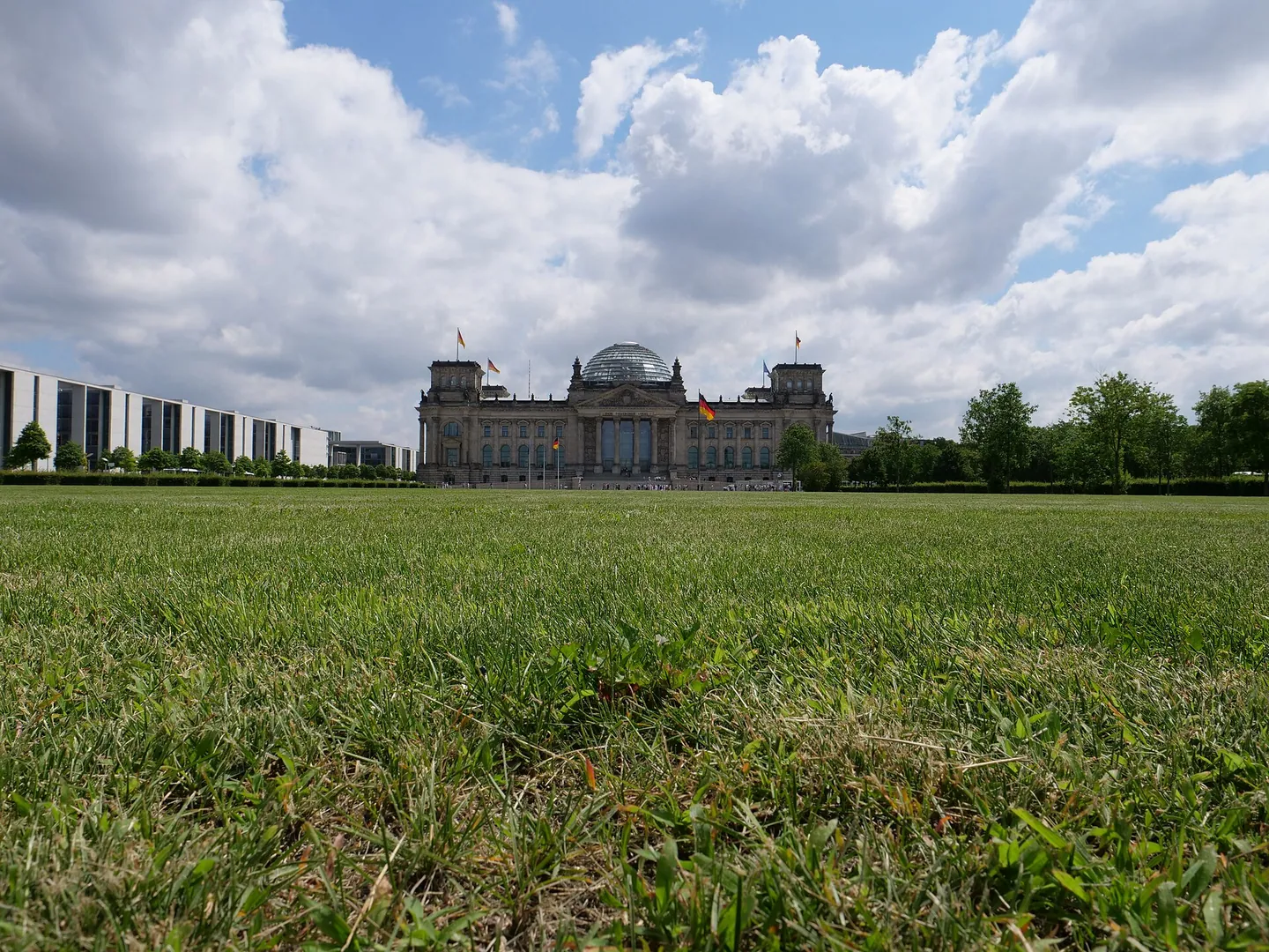 Das Reichstagsgebäude hinter einer grünen Wiese unter Wolken.