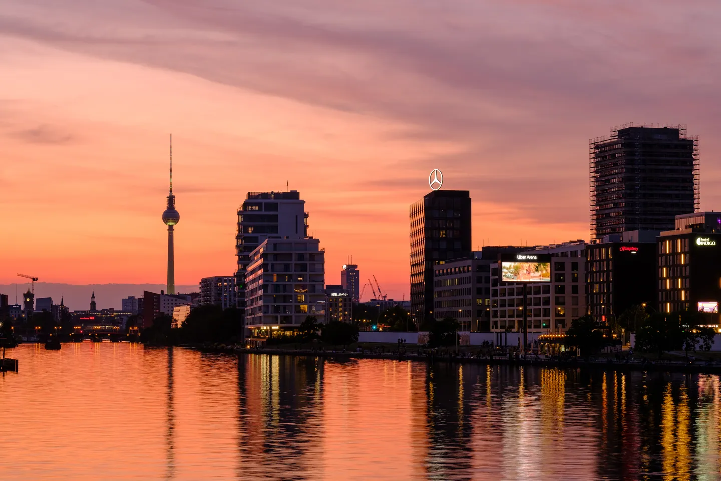 Berliner Skyline mit Fernsehturm und orangefarbenem Abendhimmel über der Spree.