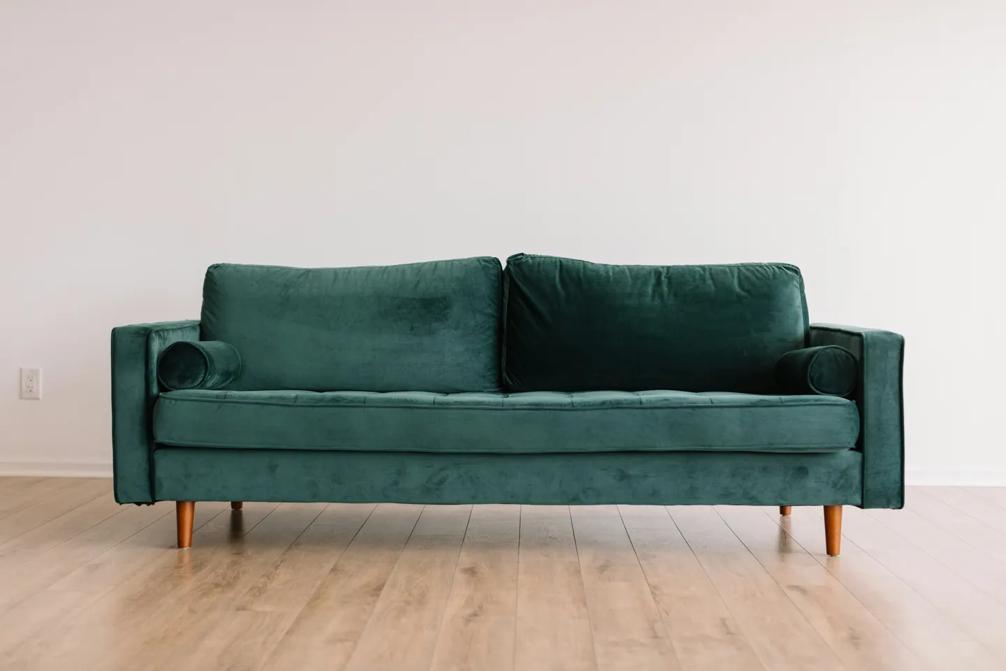 Grünes Sofa vor einer hellen Wand auf einem Holzboden.